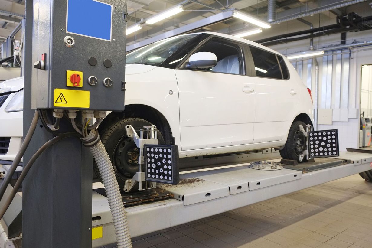 White car on an automotive alignment lift in a garage with testing equipment nearby