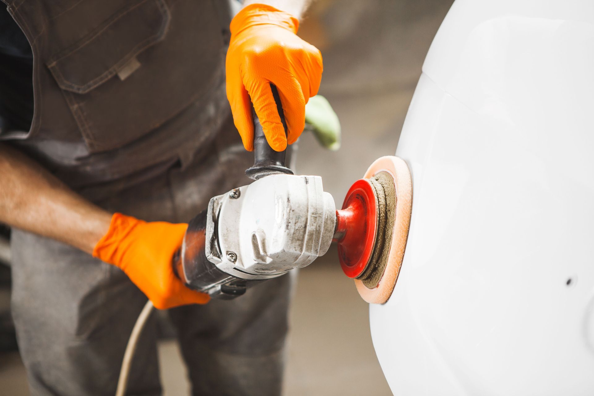 Person polishing a white car with an orbital buffer, wearing bright orange gloves