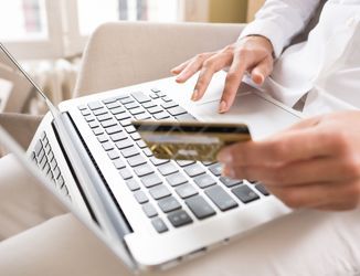 A person is holding a credit card in front of a laptop computer.