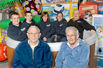 A group of seven people gathered in a retail store filled with pool and spa products, posing around a spa tub.