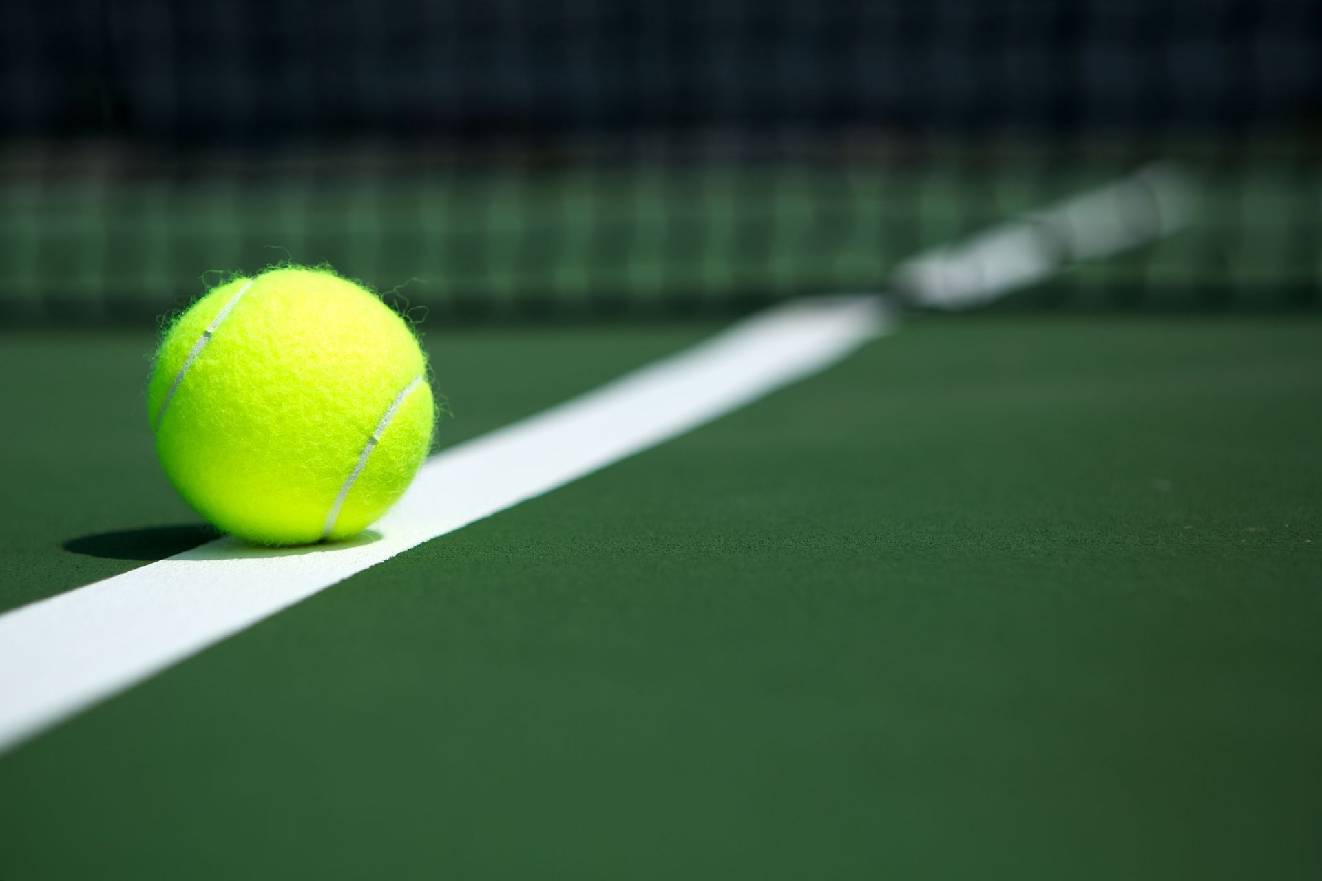 Yellow tennis ball on a green court near a white sideline
