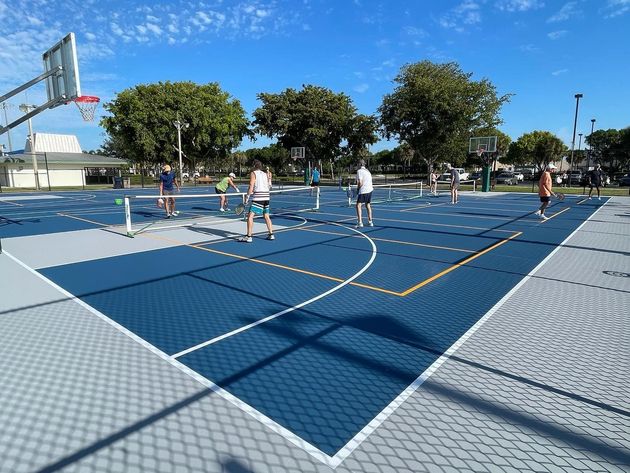 Outdoor basketball court with several people playing under a bright blue sky