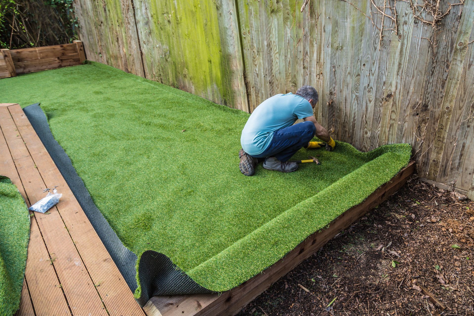 Person laying artificial grass along a backyard fence