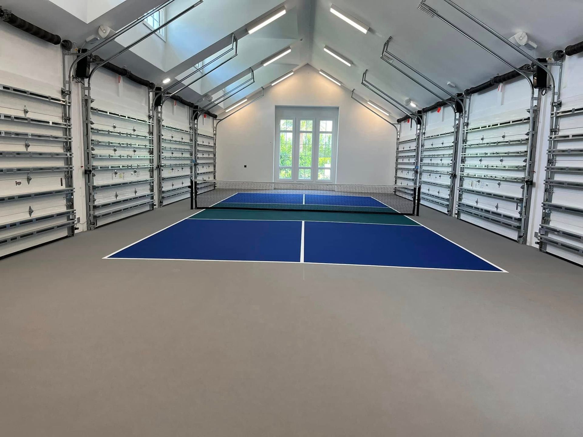 Empty indoor sports room with white walls, skylights, and a blue mat floor.