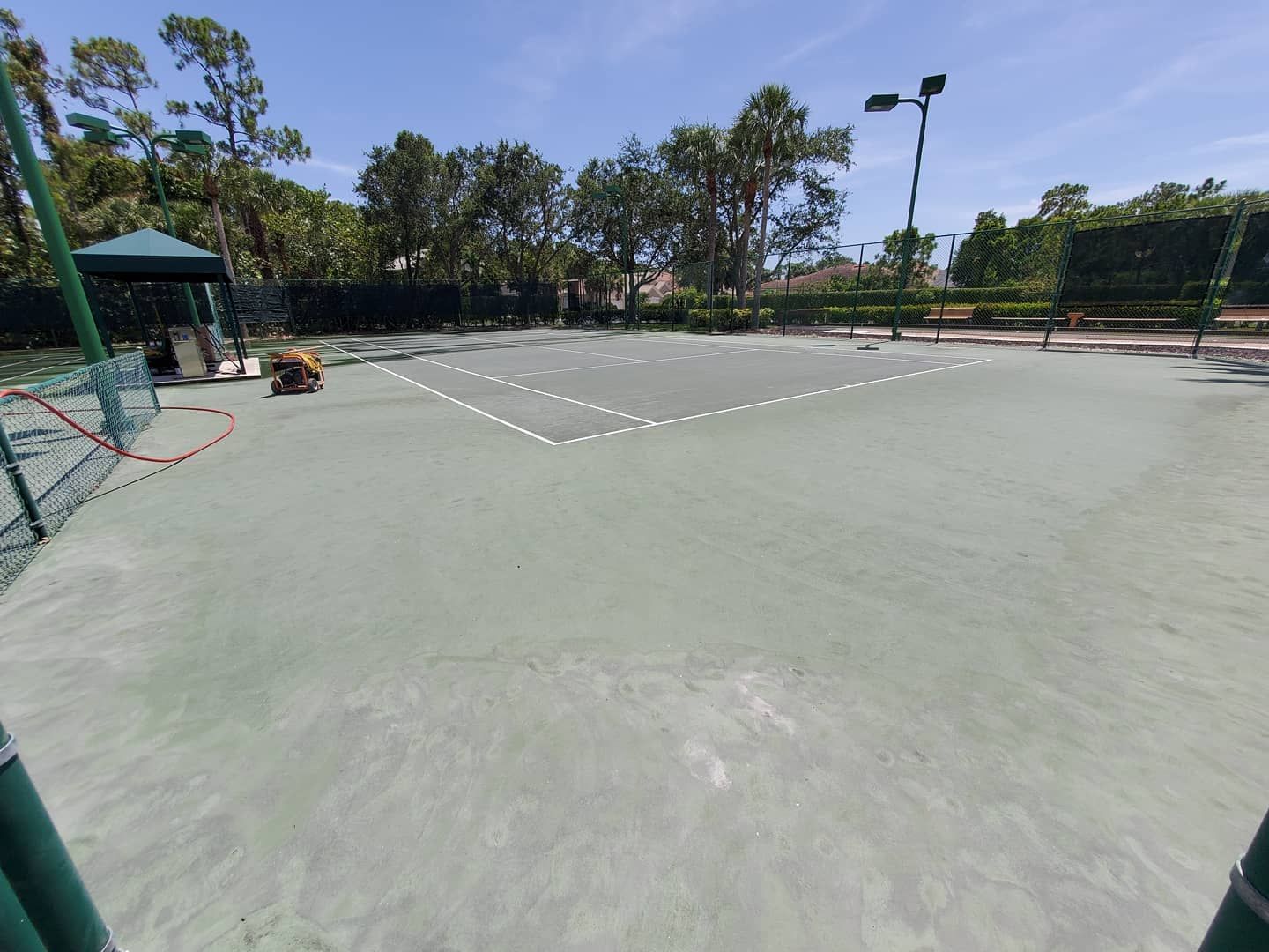 Empty outdoor tennis court with green surface, net, and trees under a sunny sky