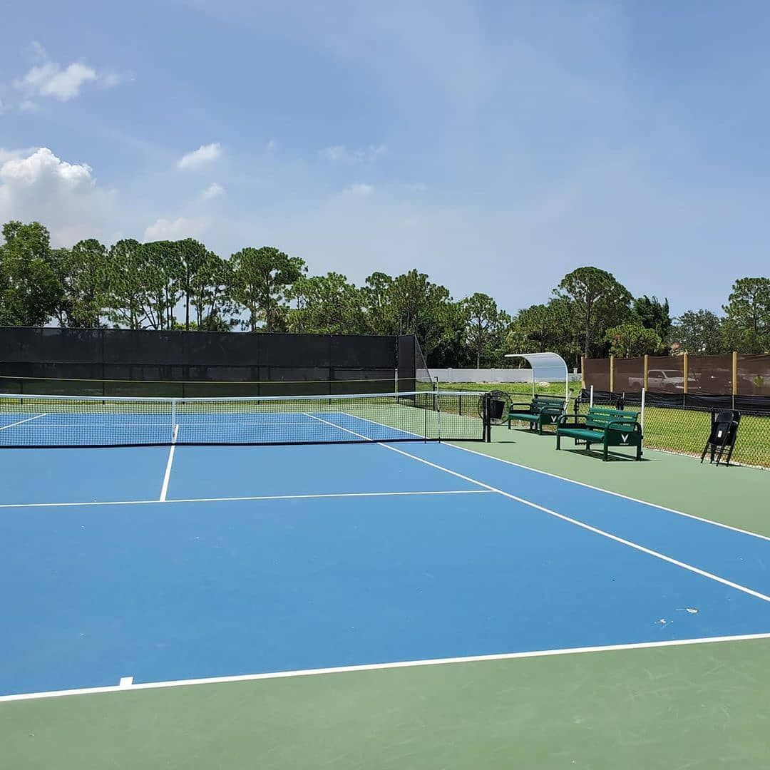 Blue tennis court under a clear sky with trees and benches along the sideline