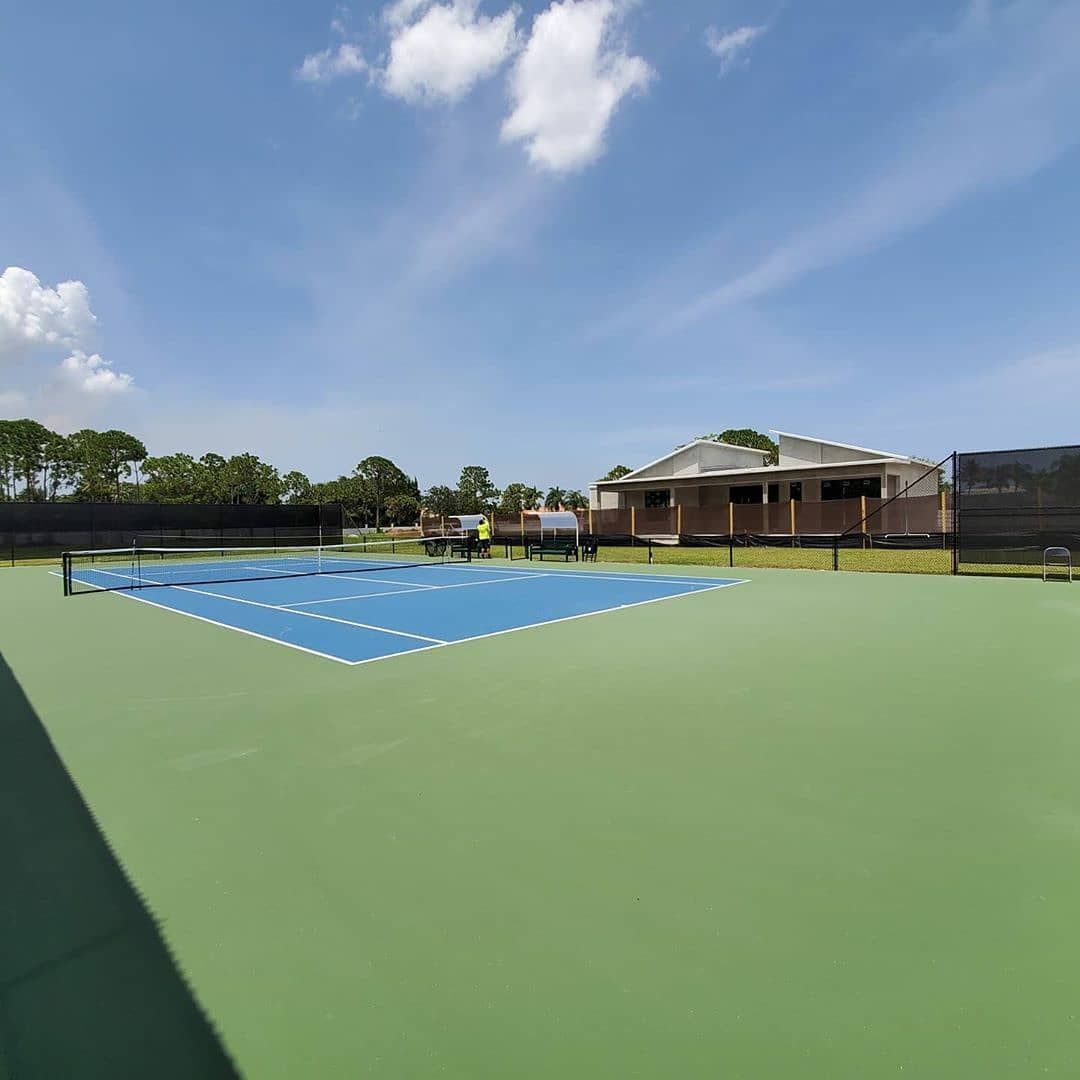 Outdoor sports court with a blue painted center on a green surface under a clear sky