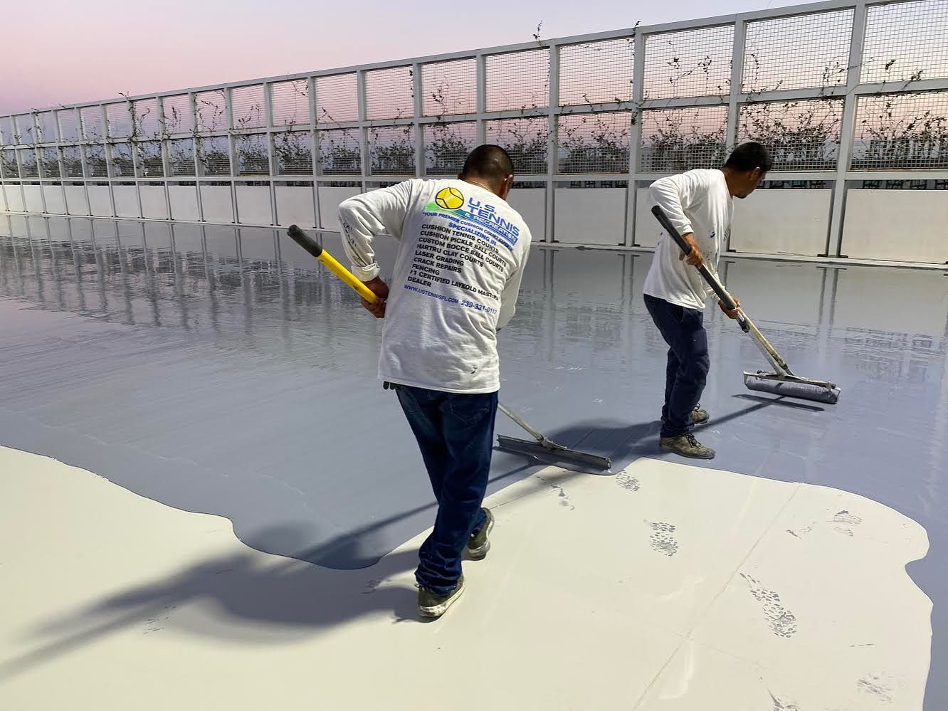 Two workers painting a large rooftop, one using a roller and one a long-handled applicator