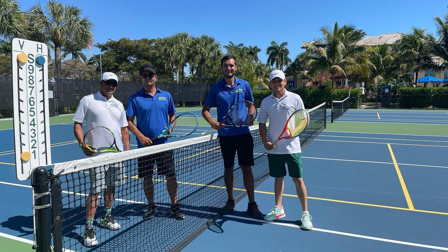 Four people stand at a pickleball net on a blue court, holding paddles in bright sunlight.