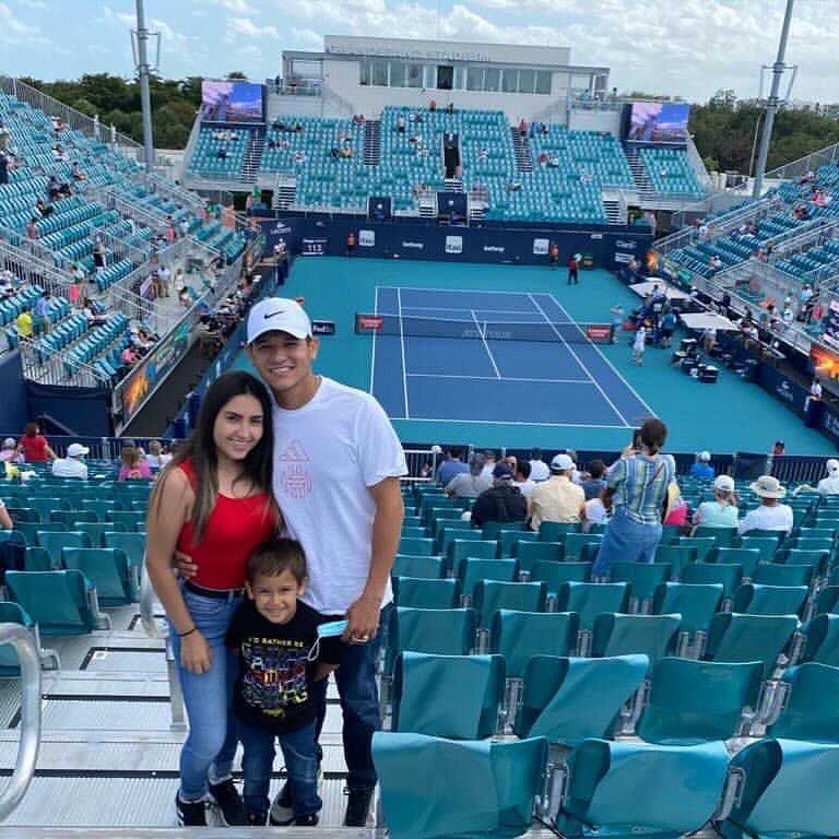 Family posing in stadium seats overlooking a blue tennis court during a match