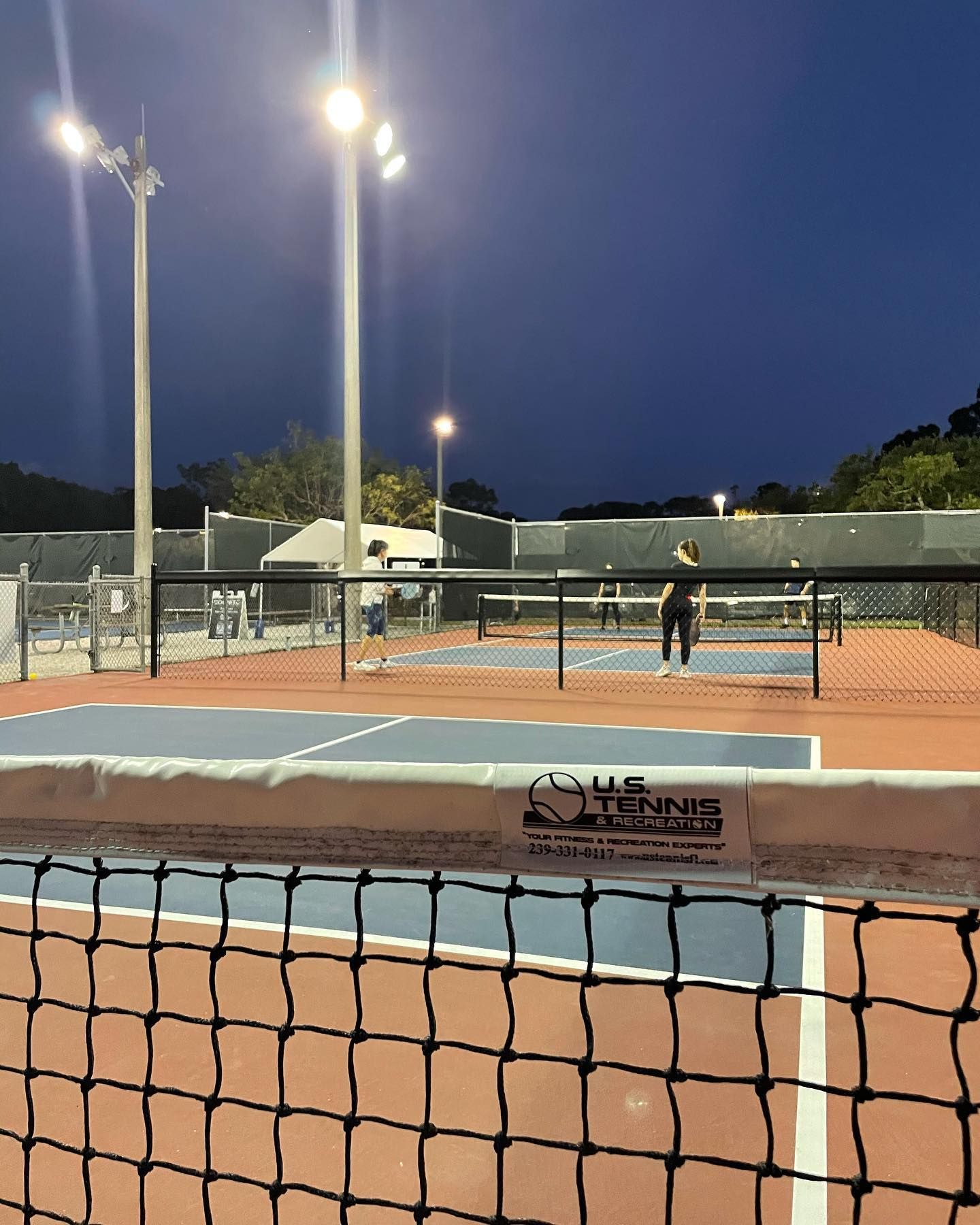 Nighttime tennis court with two players and bright floodlights