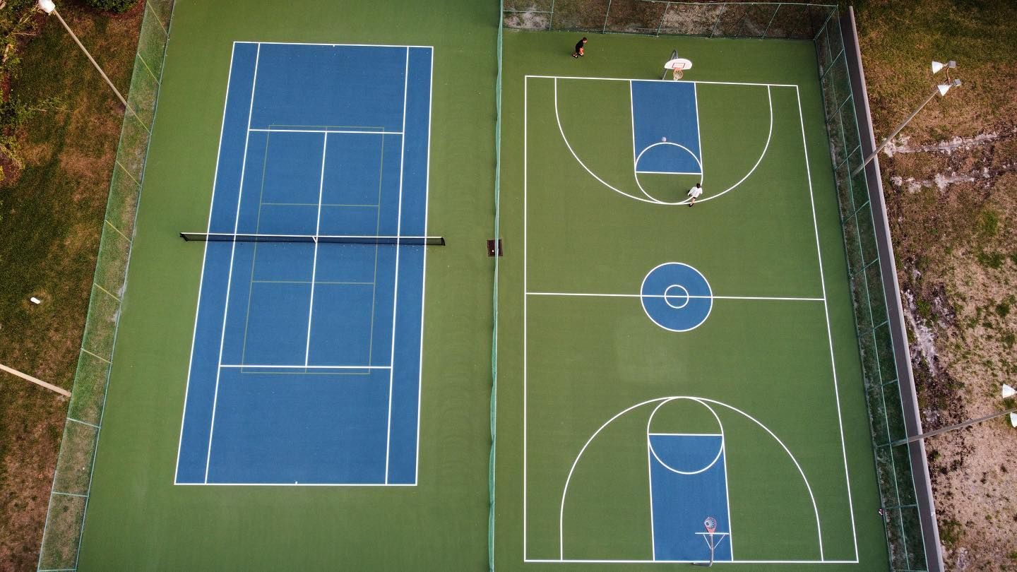 Aerial view of two adjacent outdoor basketball courts, one blue and one green, surrounded by trees.