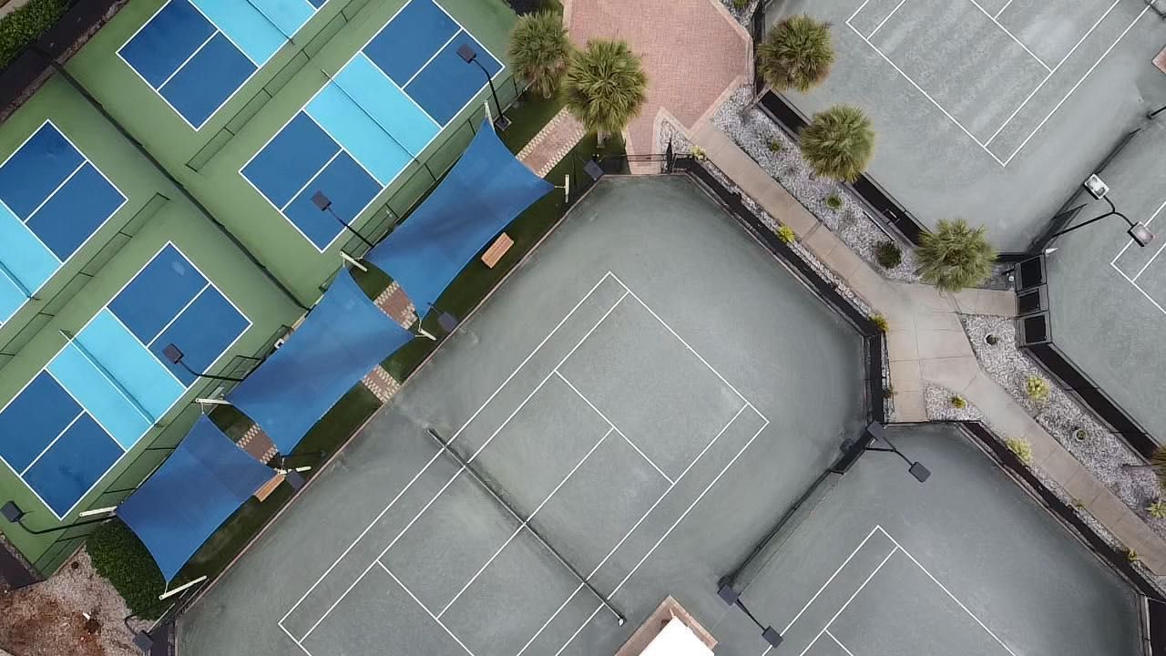 Aerial view of tennis and pickleball courts beside a parking lot and paved walkway