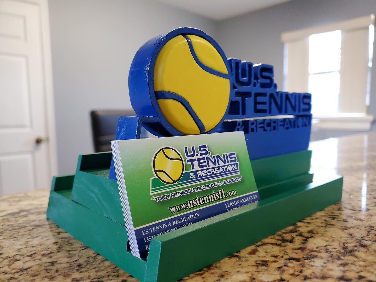 US Tennis trophy with blue-and-yellow tennis ball logo on green base indoors