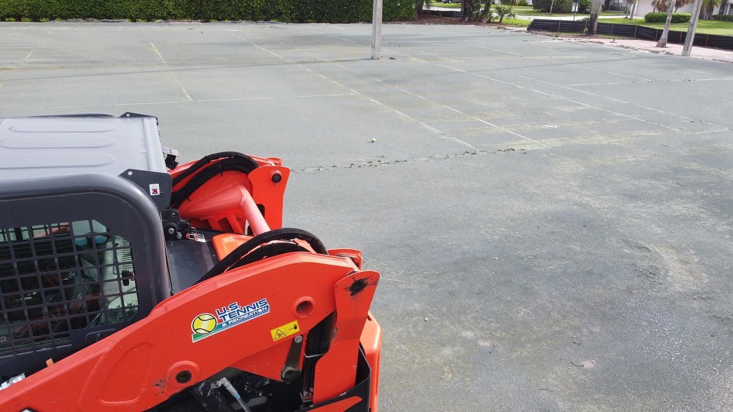 Red construction machine parked on asphalt lot with a red bag or toolbox attached