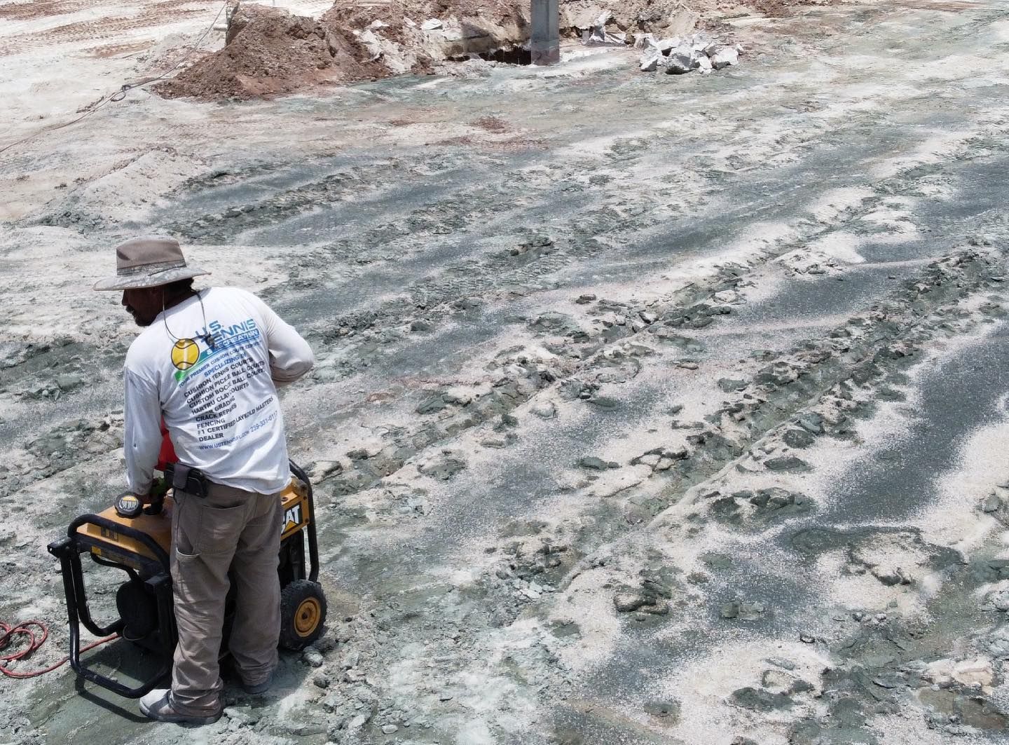 Person in a hat operating a small machine on a muddy outdoor surface.