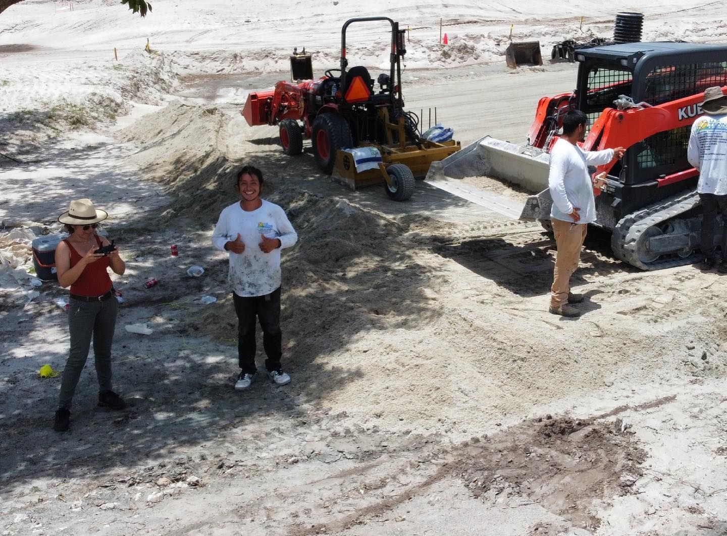 People standing beside construction equipment on a muddy worksite.