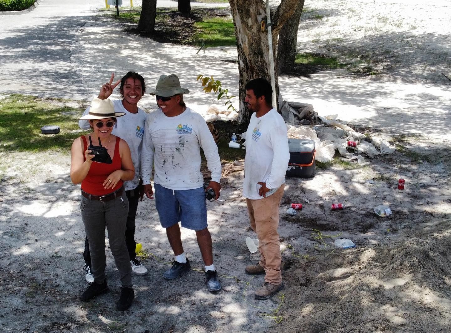 Four people standing outdoors on a sandy path, smiling and posing in the shade.