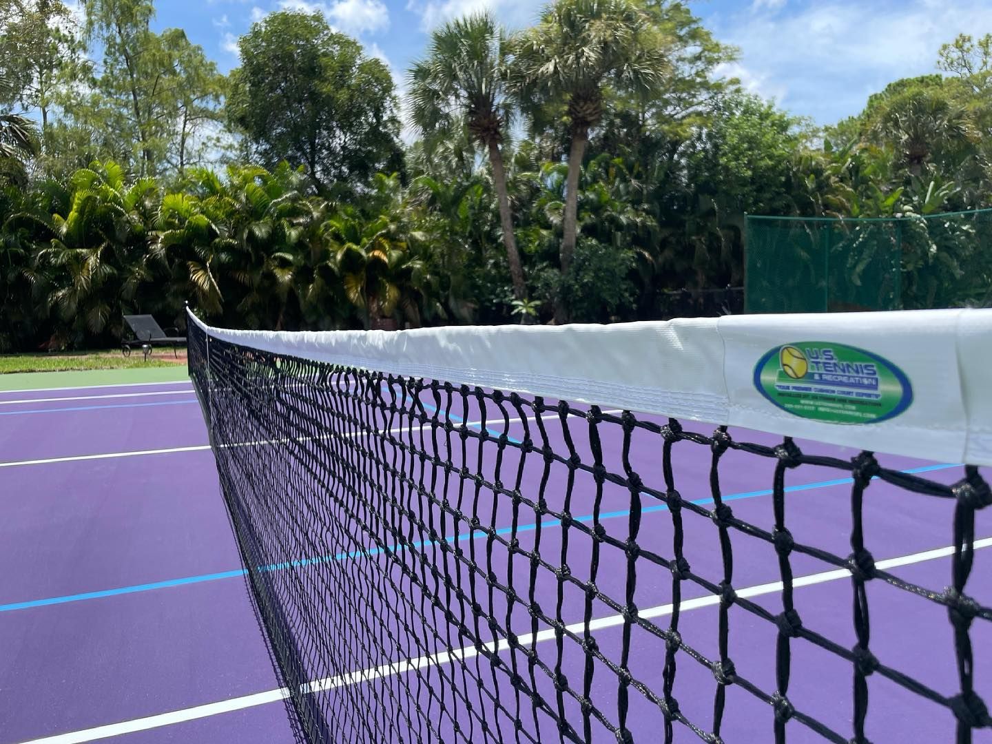 Purple tennis court with a net in the foreground and trees beyond the fence