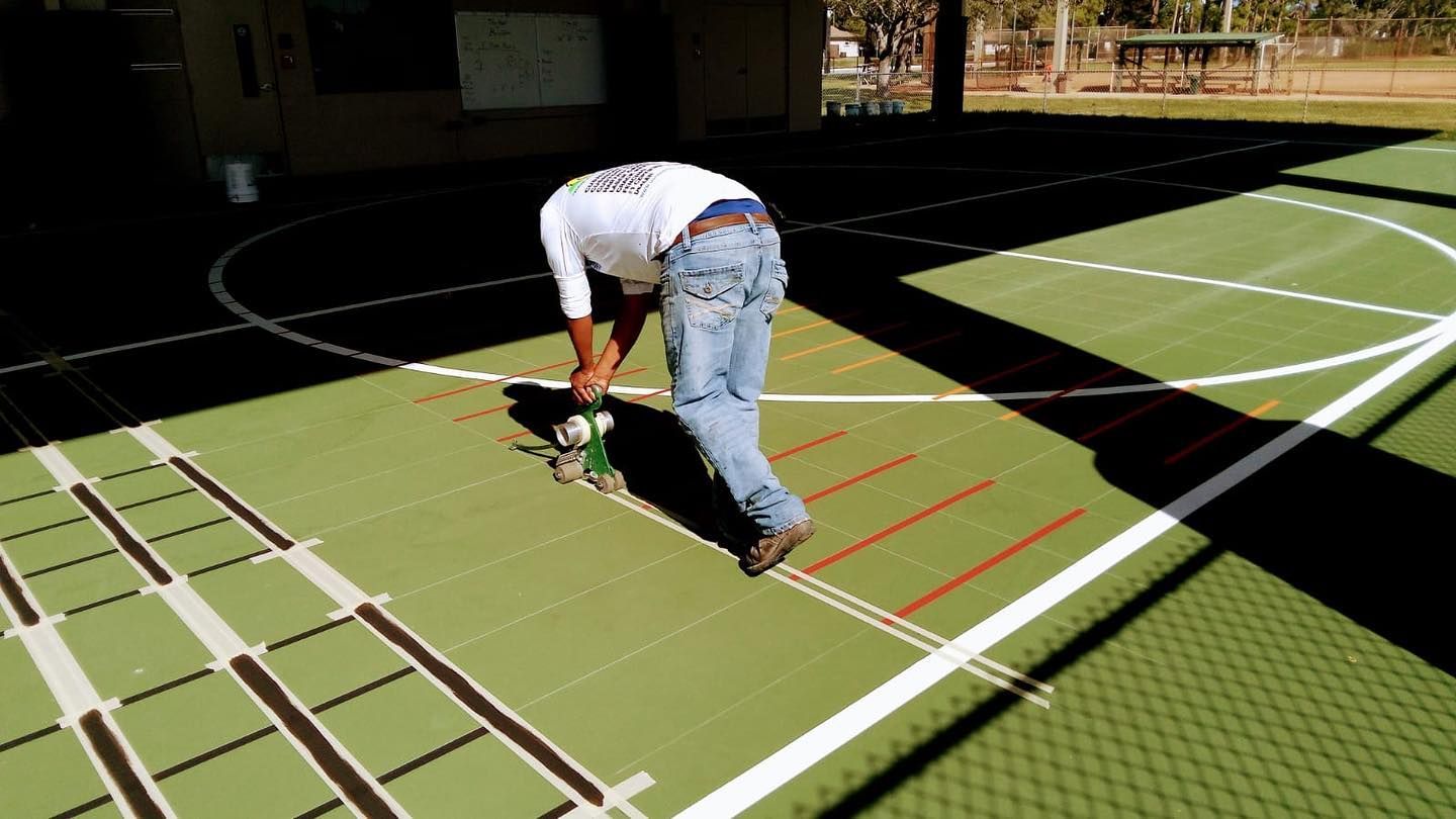 Person kneeling on a green sports court beside a white ladder drill and red agility lines