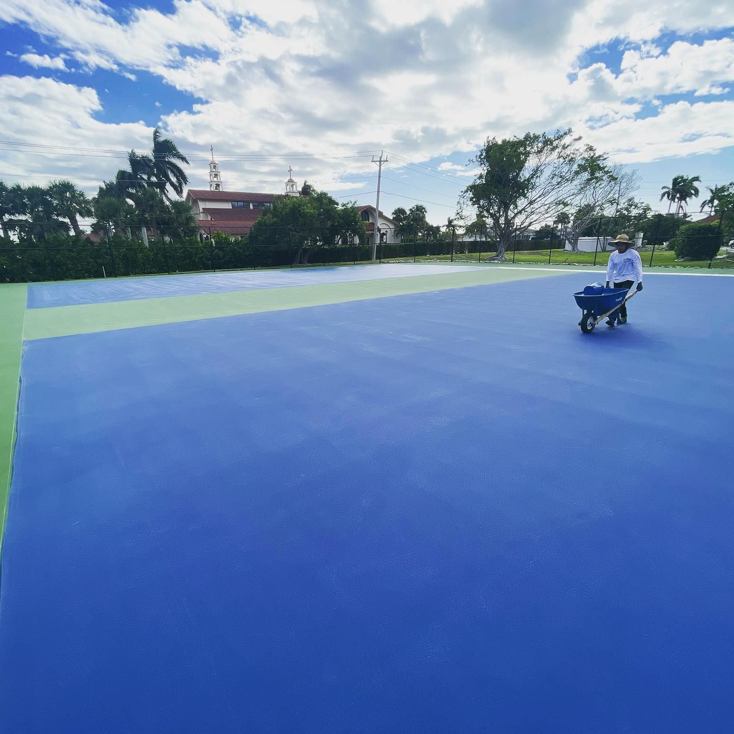 Person on a scooter on a blue sports court under a cloudy sky