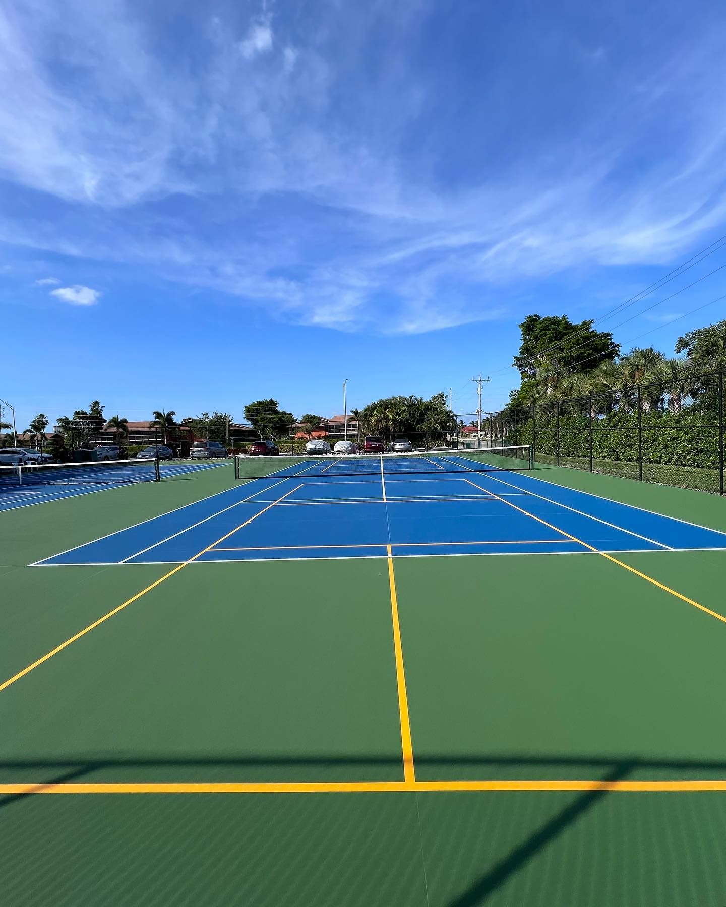 Empty outdoor tennis court with blue and green surfaces under a bright blue sky