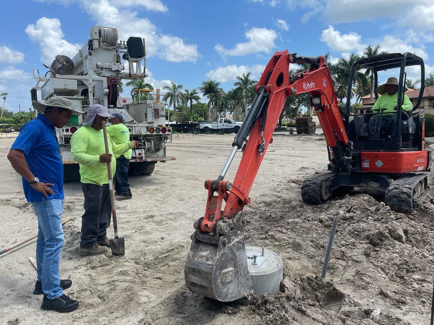 Workers and a red excavator on a muddy construction site beside a large drilling rig