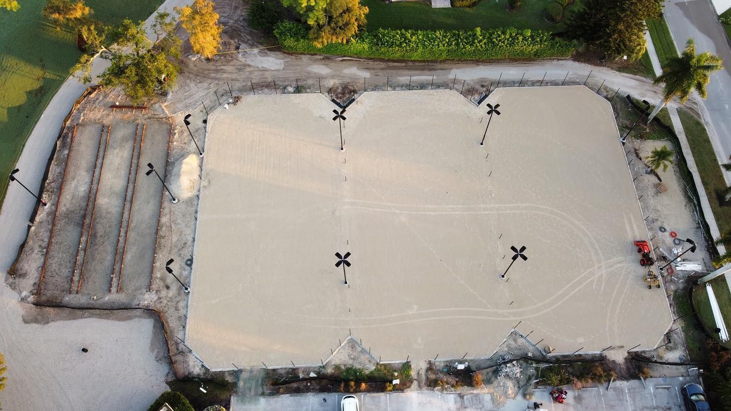 Aerial view of a large empty sand court bordered by trees and steps on one side.