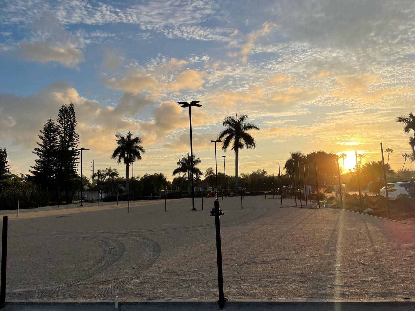 Sunset over a sandy court with palm trees and a fence silhouetted against the sky