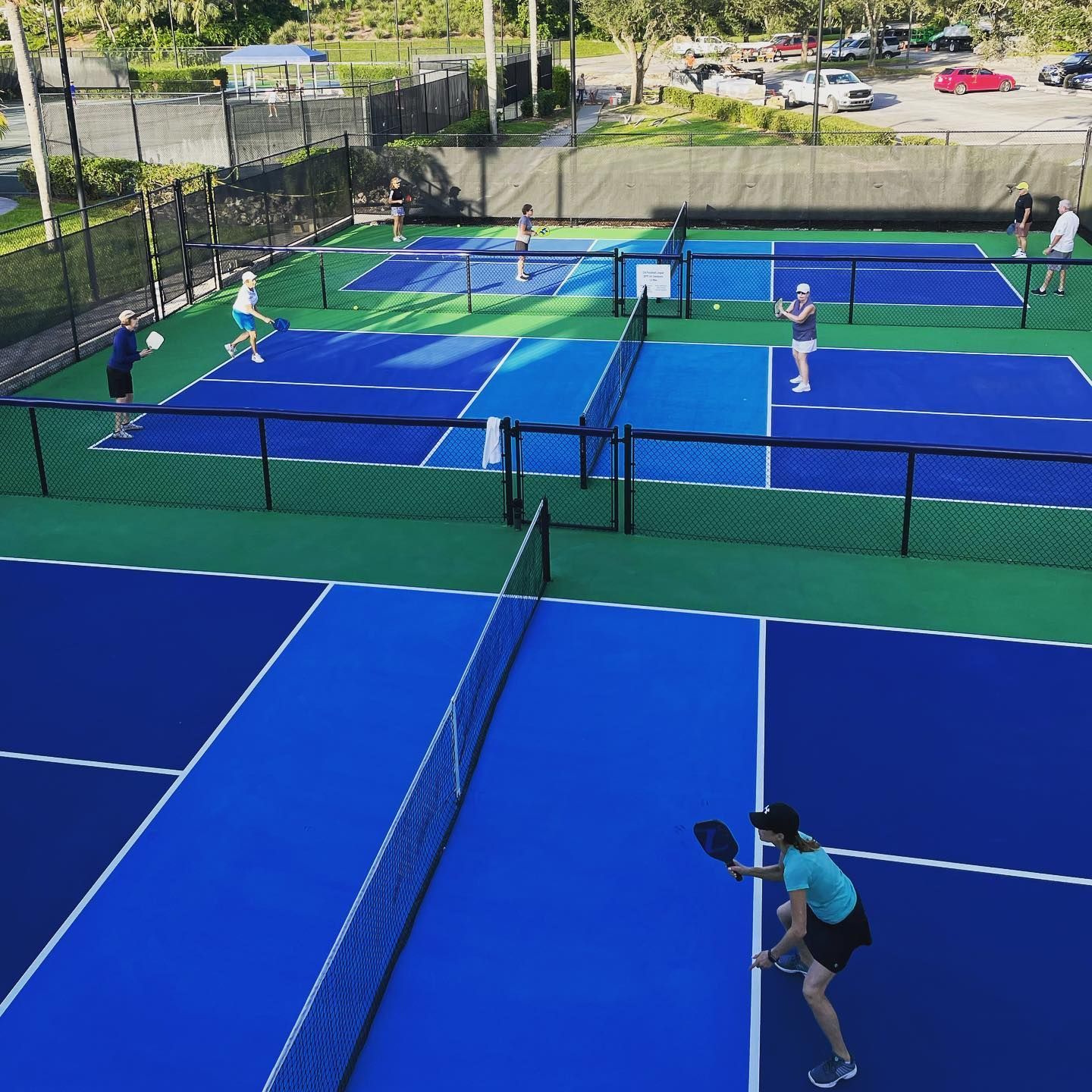 Pickleball courts with players on bright blue outdoor courts, viewed from above