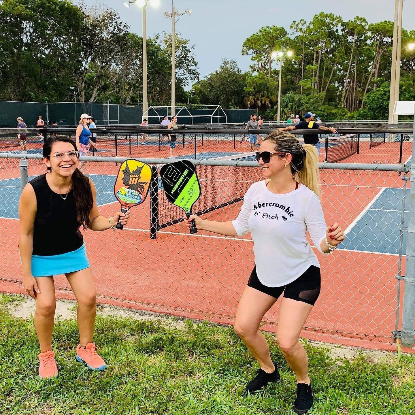 Two people posing with pickleball paddles on an outdoor court, smiling and ready to play.