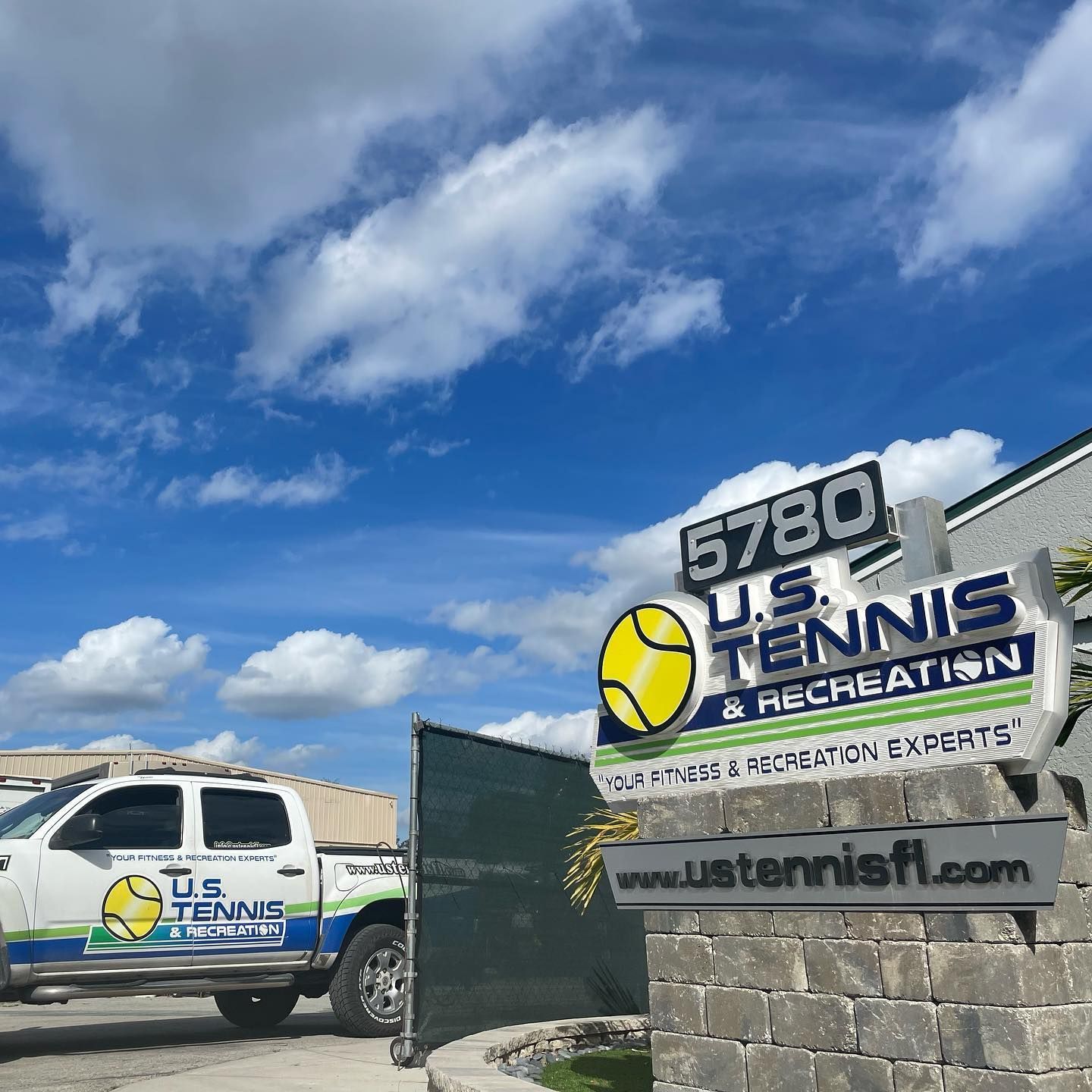 US Tennis & Recreation storefront sign and van under a blue sky