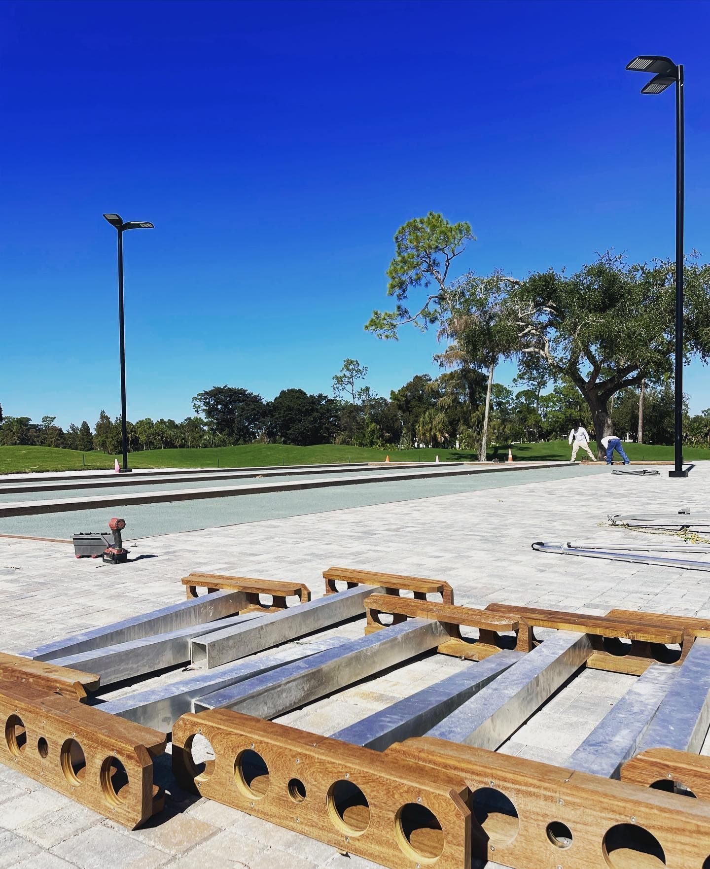 Outdoor park with a wooden play structure under a clear blue sky, with a few people in the distance