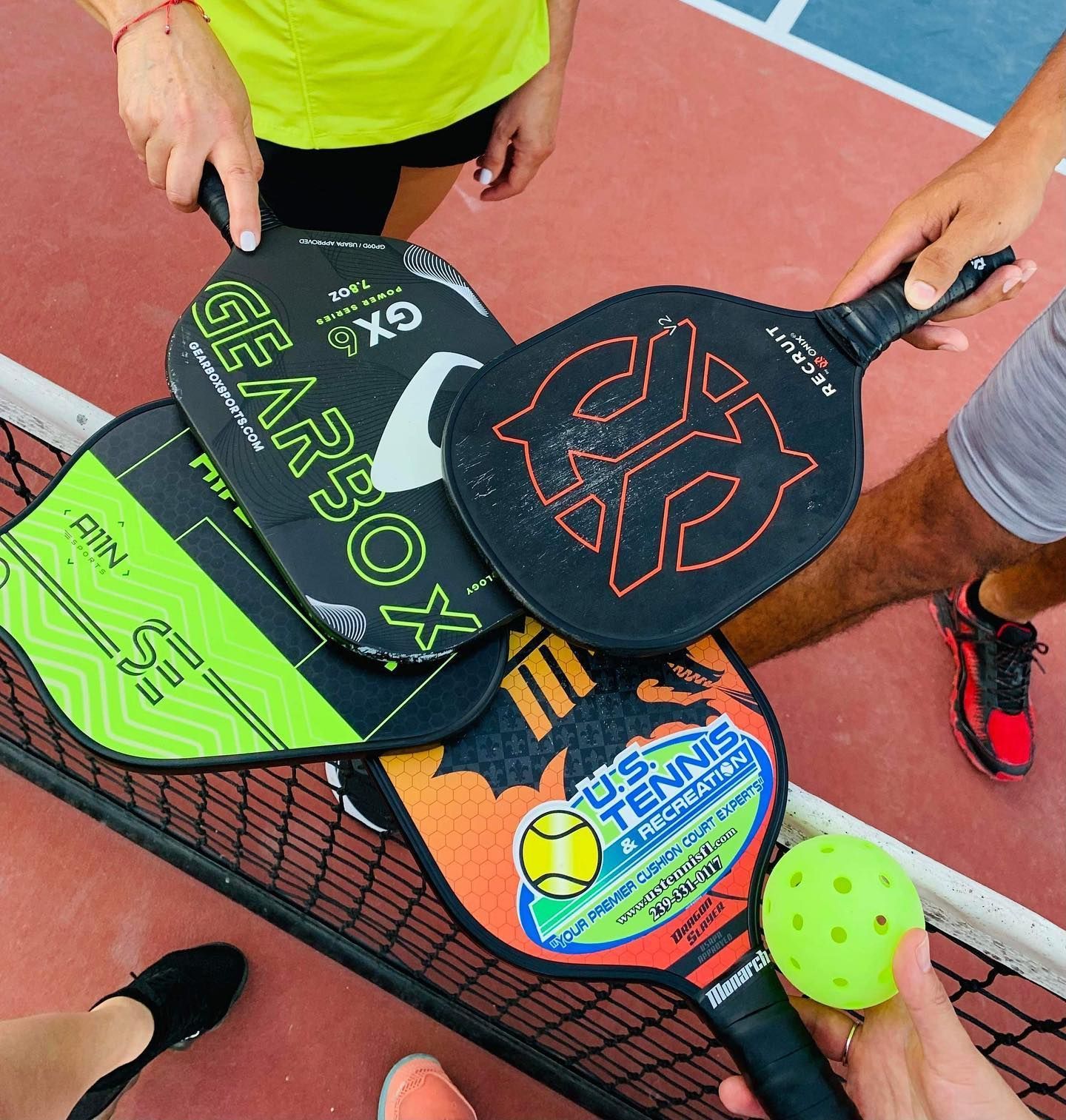 Three pickleball paddles and a ball held over an outdoor court