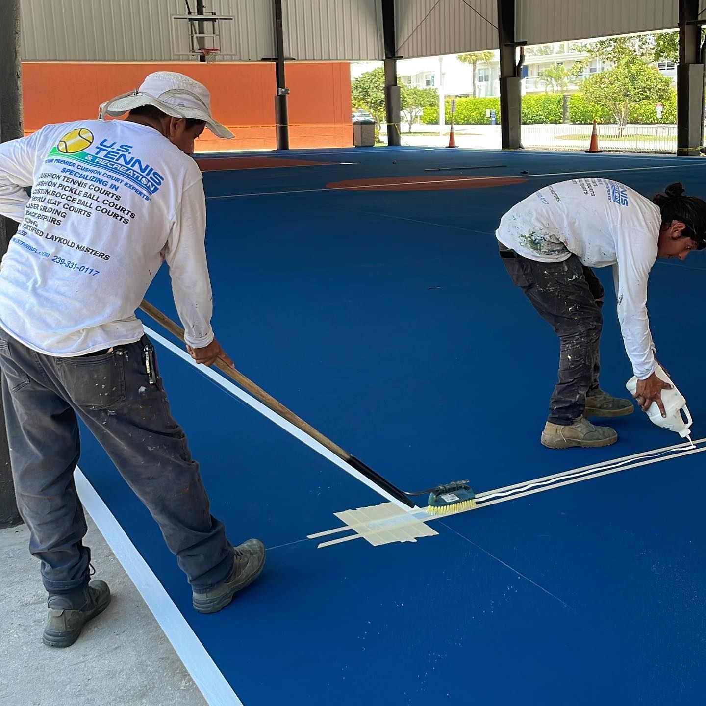 Two workers painting white lines on a blue indoor sports court