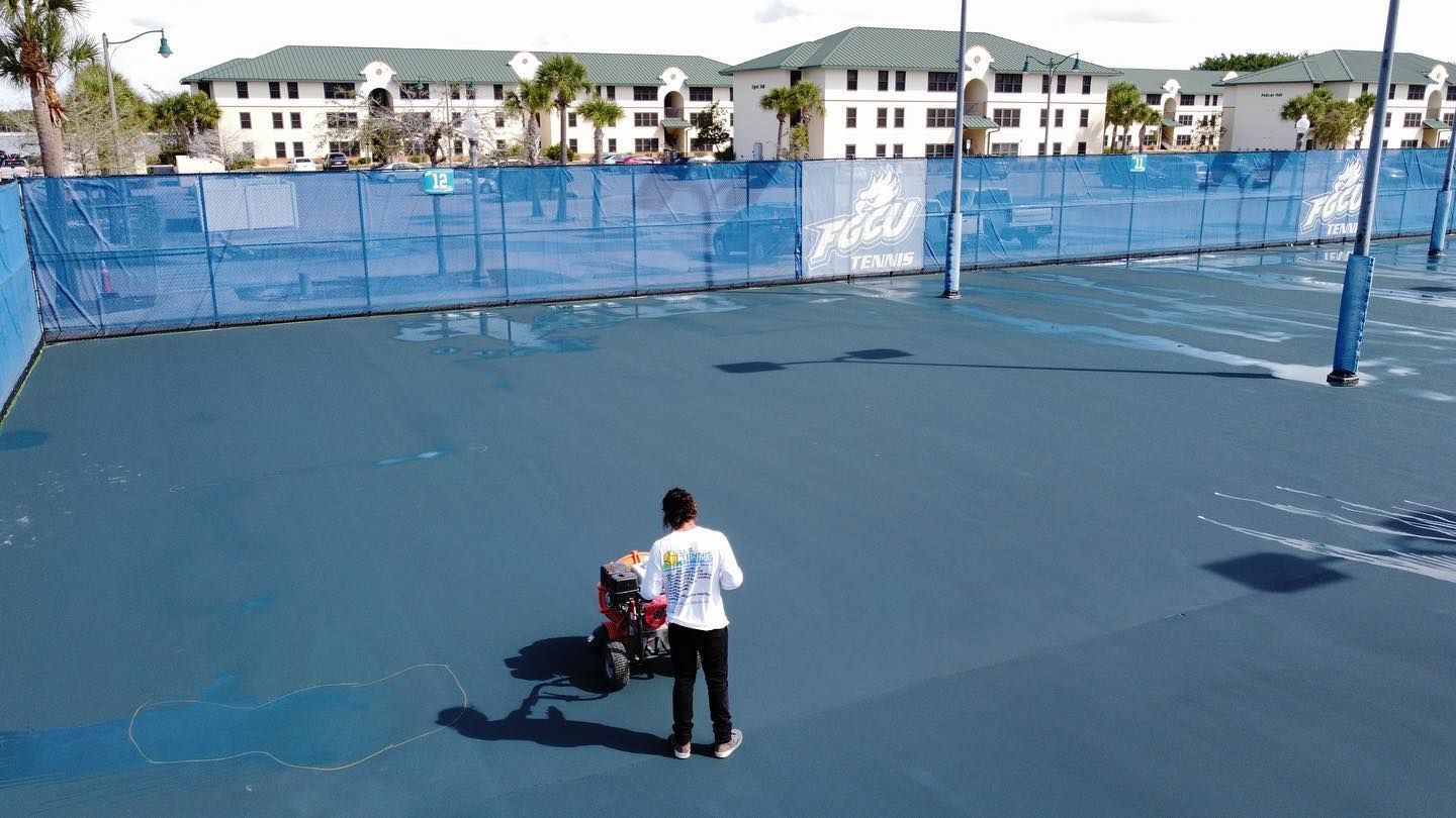 Person with luggage on a blue tennis court near a fenced apartment complex