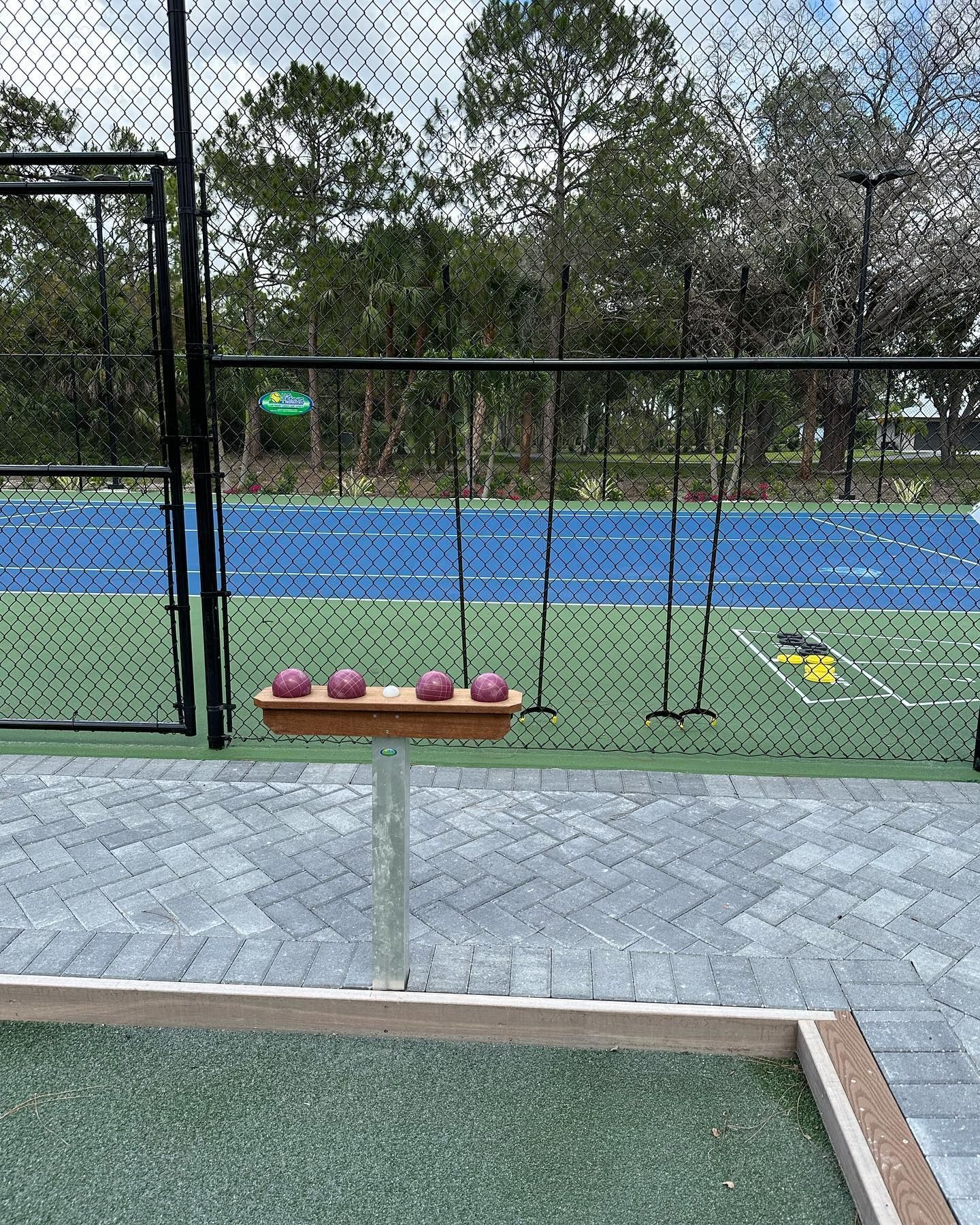 Outdoor tennis court with four pink balls on a small stand near the net, rackets hanging nearby.