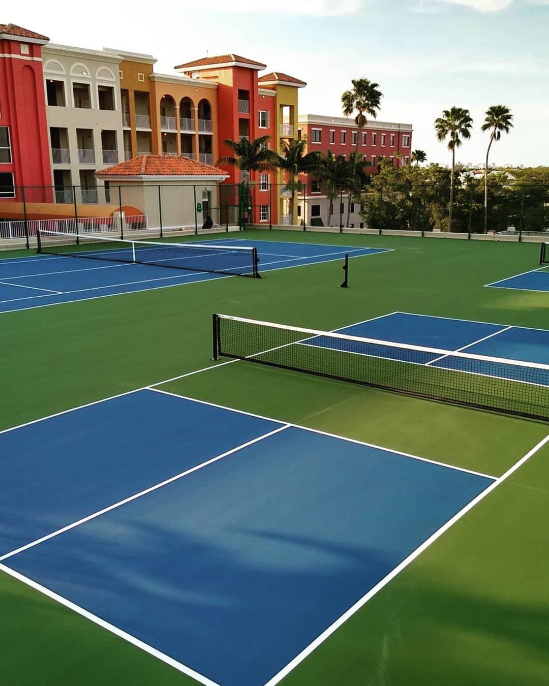 Empty blue tennis courts beside a red resort building with palm trees