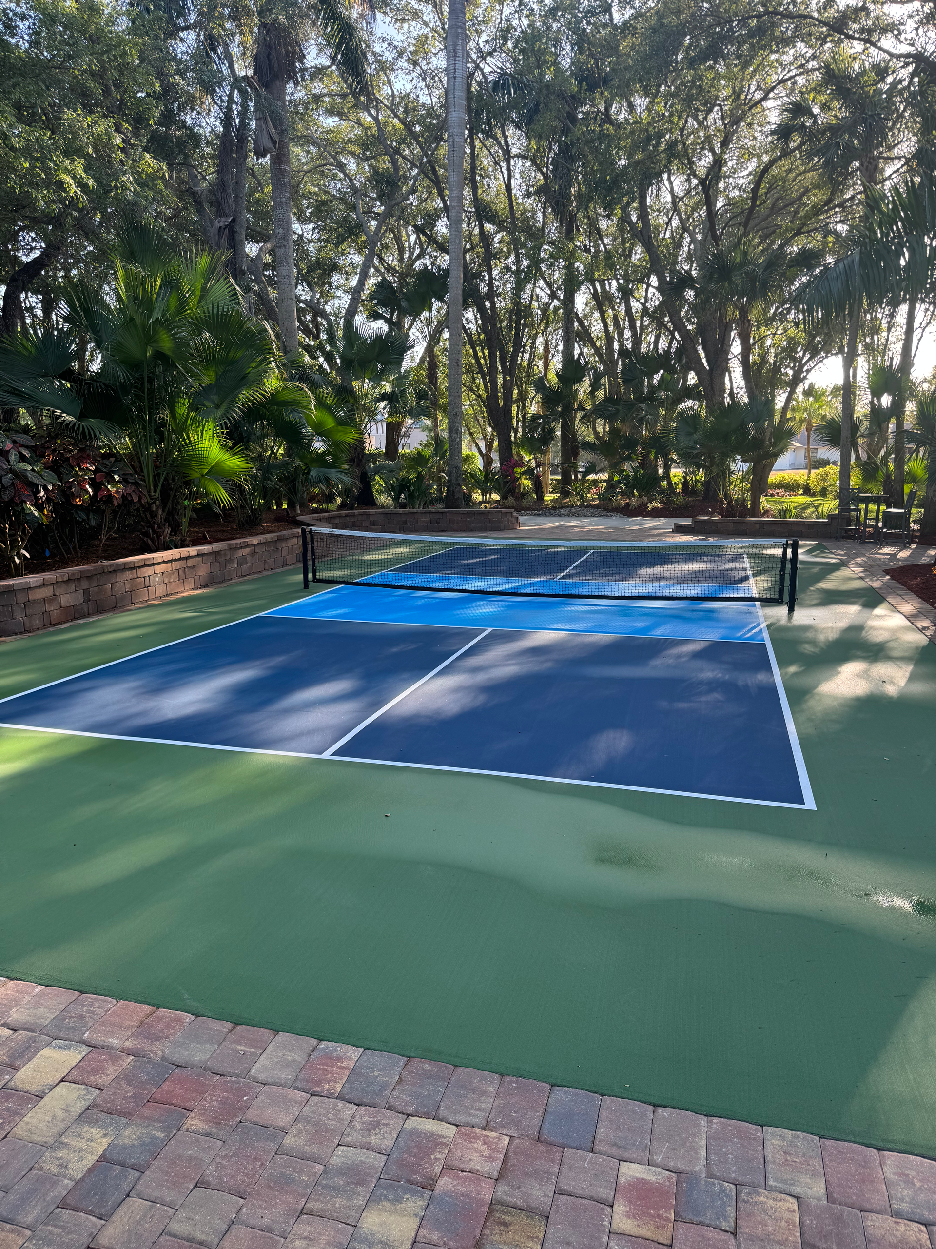 Outdoor blue tennis court surrounded by trees and a brick walkway