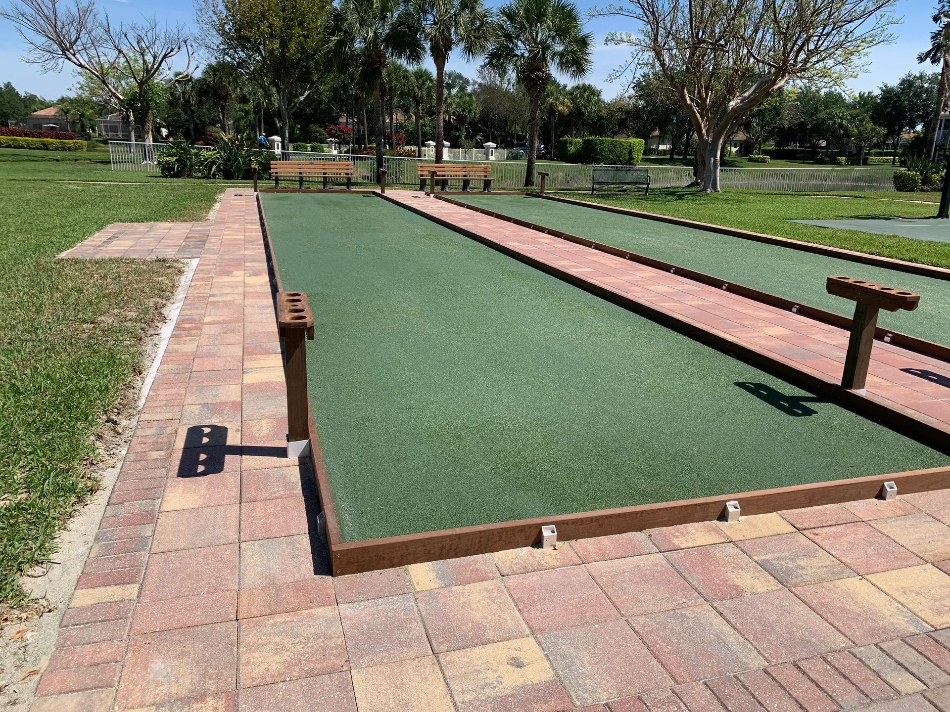 Outdoor bocce court with green turf lanes, brick borders, and trees in a park setting