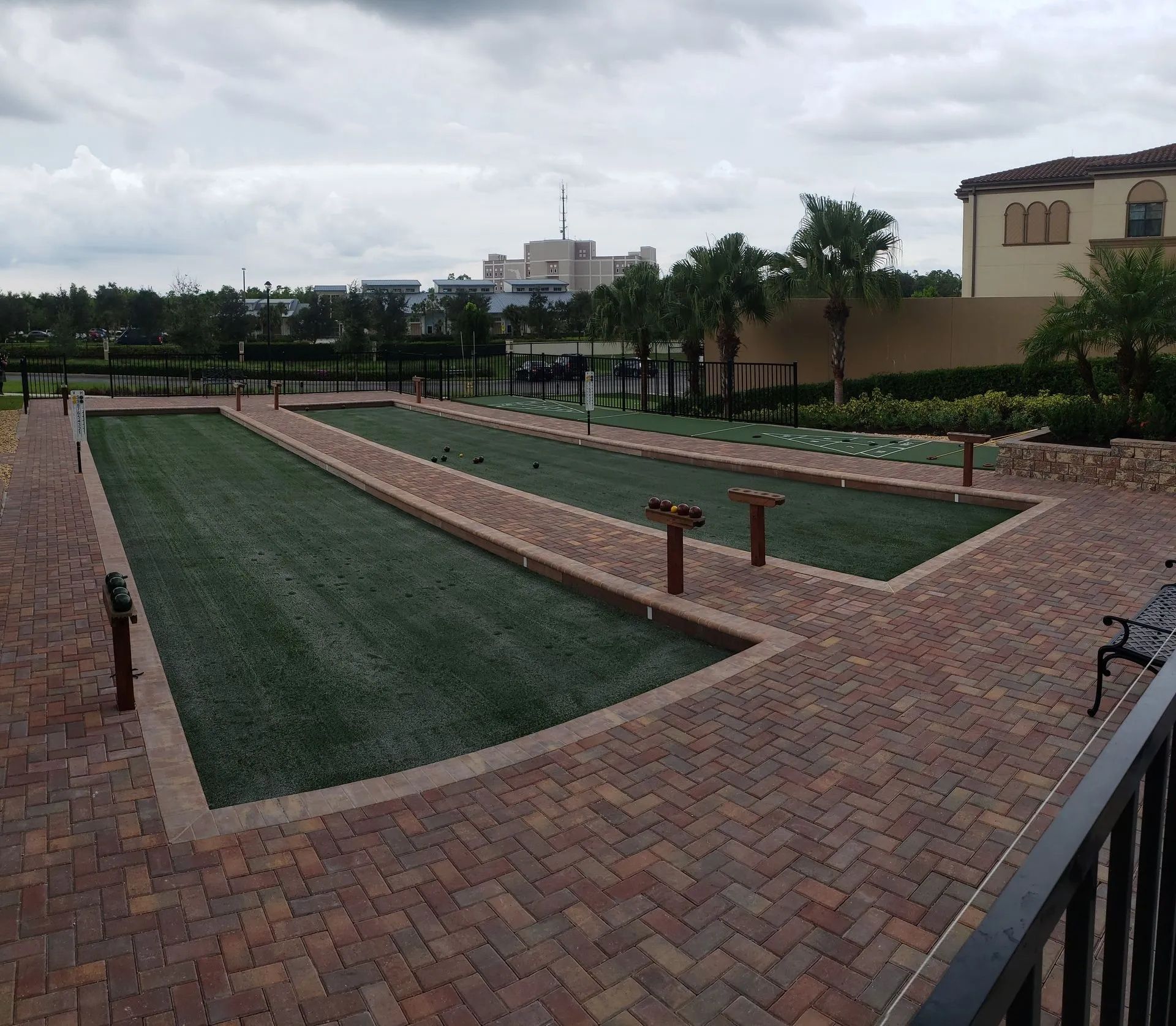 Brick-bordered outdoor miniature golf course with green turf lanes under a cloudy sky