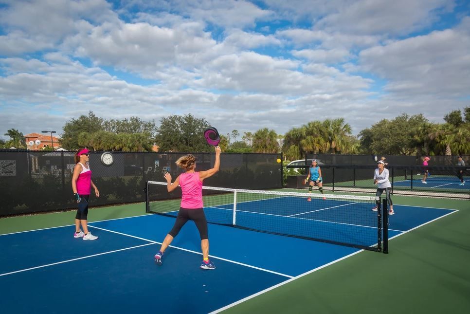 People playing pickleball on outdoor blue courts under a cloudy sky