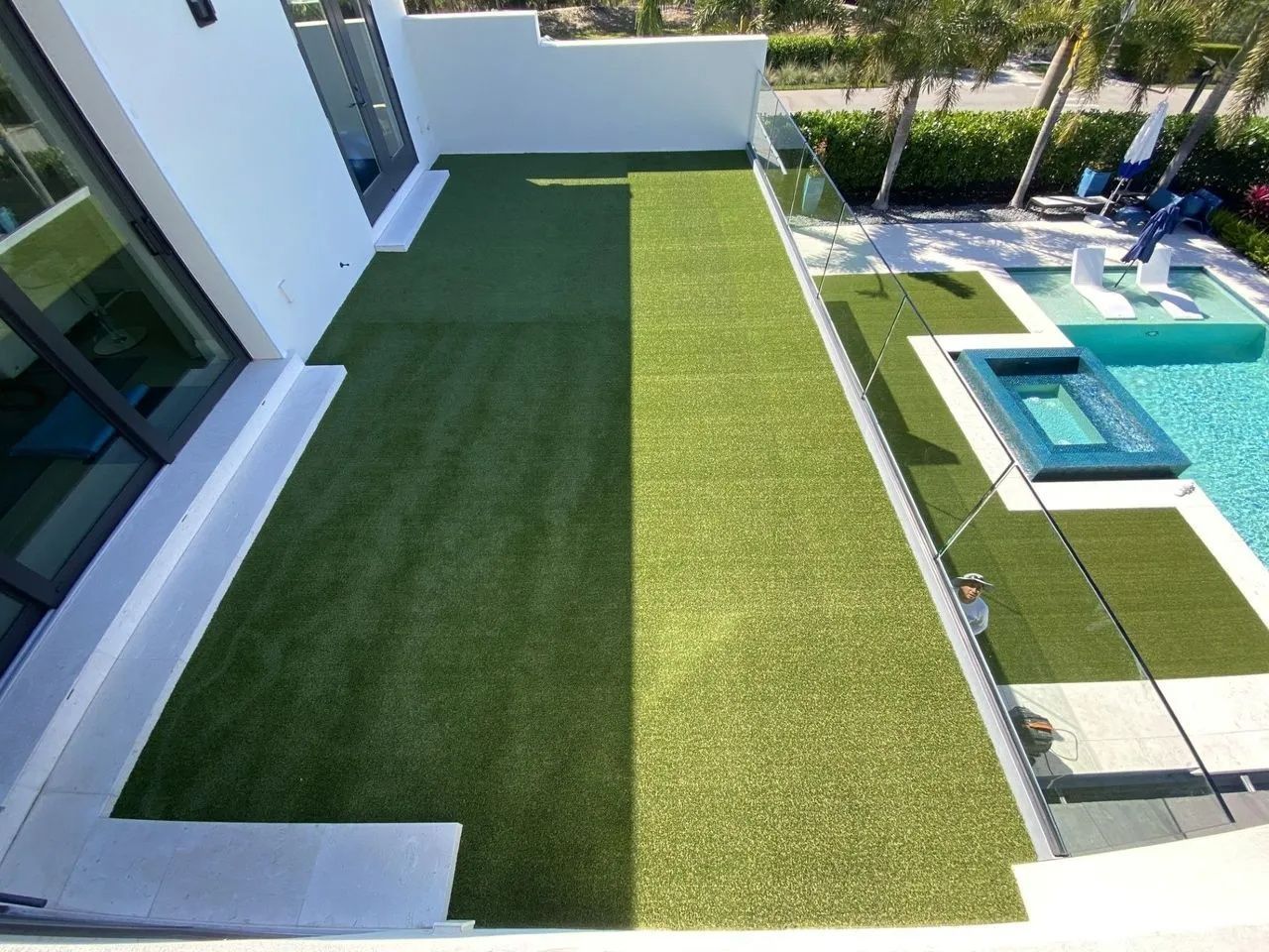 Modern backyard patio with artificial grass, white walls, and a turquoise pool deck.