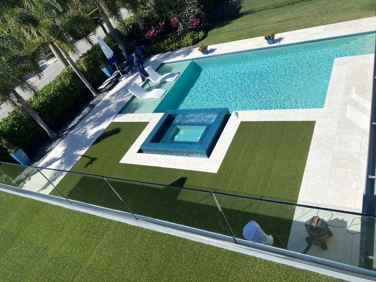 Modern backyard pool with turquoise water, small spa, and green lawn beside a glass fence