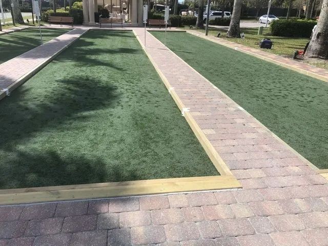 Outdoor park with two green artificial-turf lanes bordered by brick walkways and trees