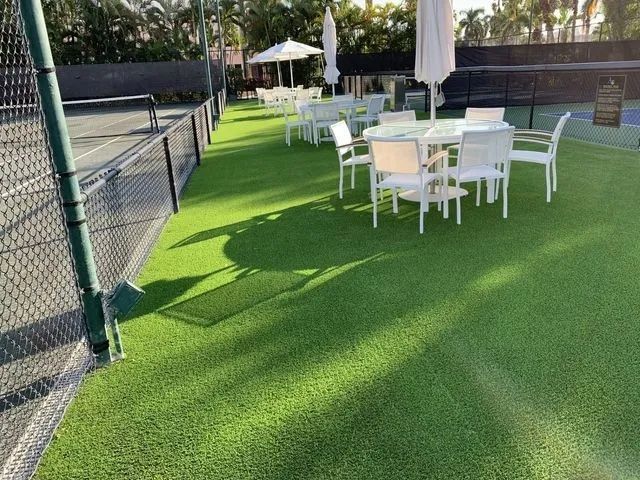 Outdoor patio with white tables and chairs on bright green artificial turf beside a fence.