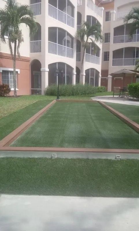 Courtyard with a central green lawn path between beige apartment buildings and palm trees