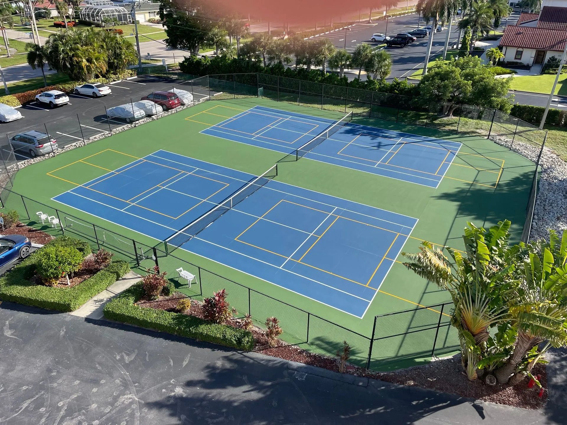 Blue and green outdoor tennis/pickleball courts beside a parking lot and trees