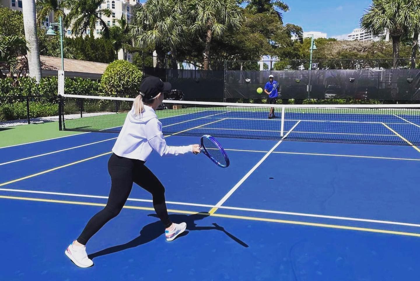 Person playing tennis on a blue outdoor court, mid-swing near the net.