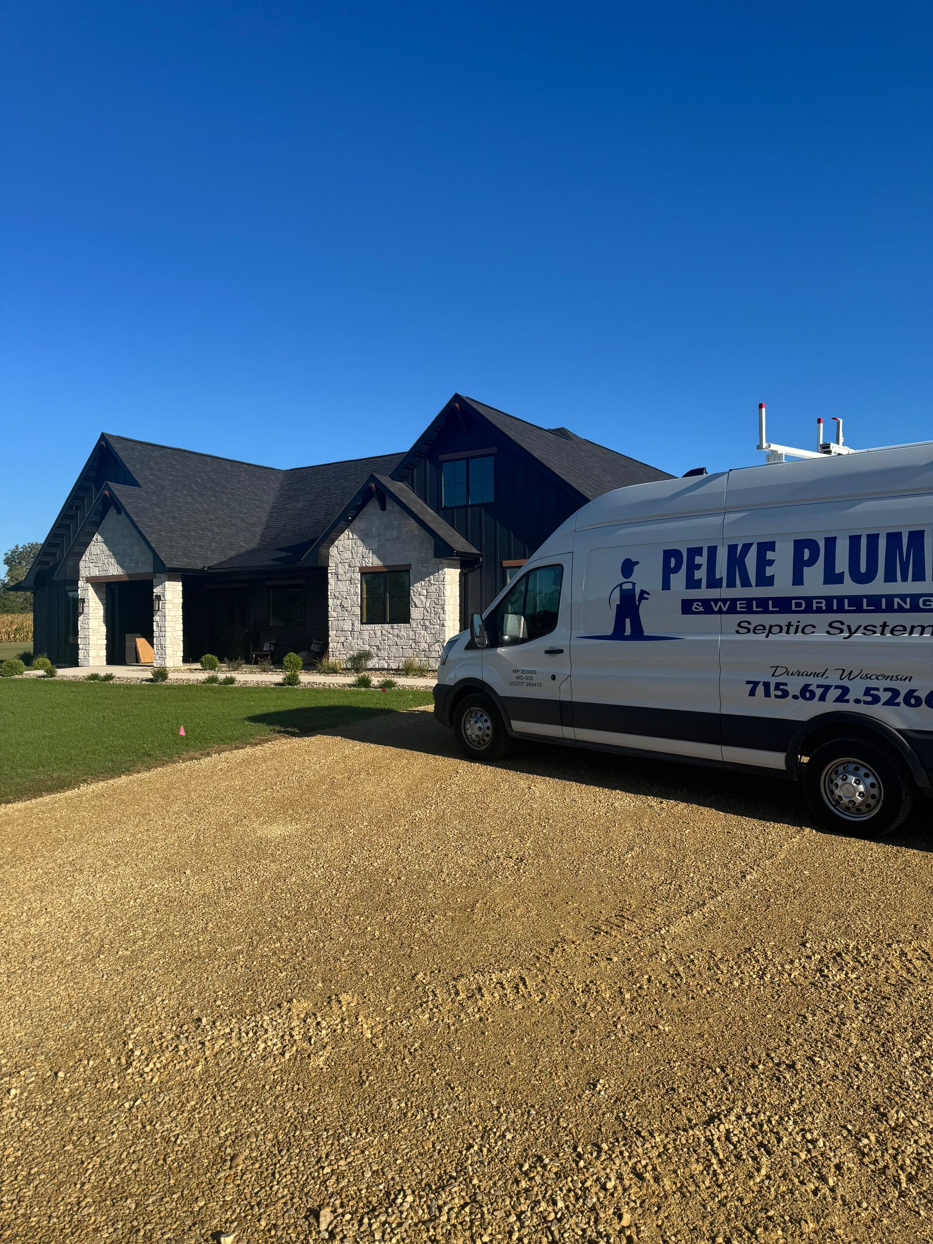 White service van in a gravel driveway beside a stone house under a clear blue sky